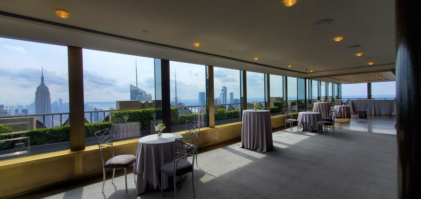 An event space high above Manhattan set with cocktail tables, looking out towards the Empire State Building.